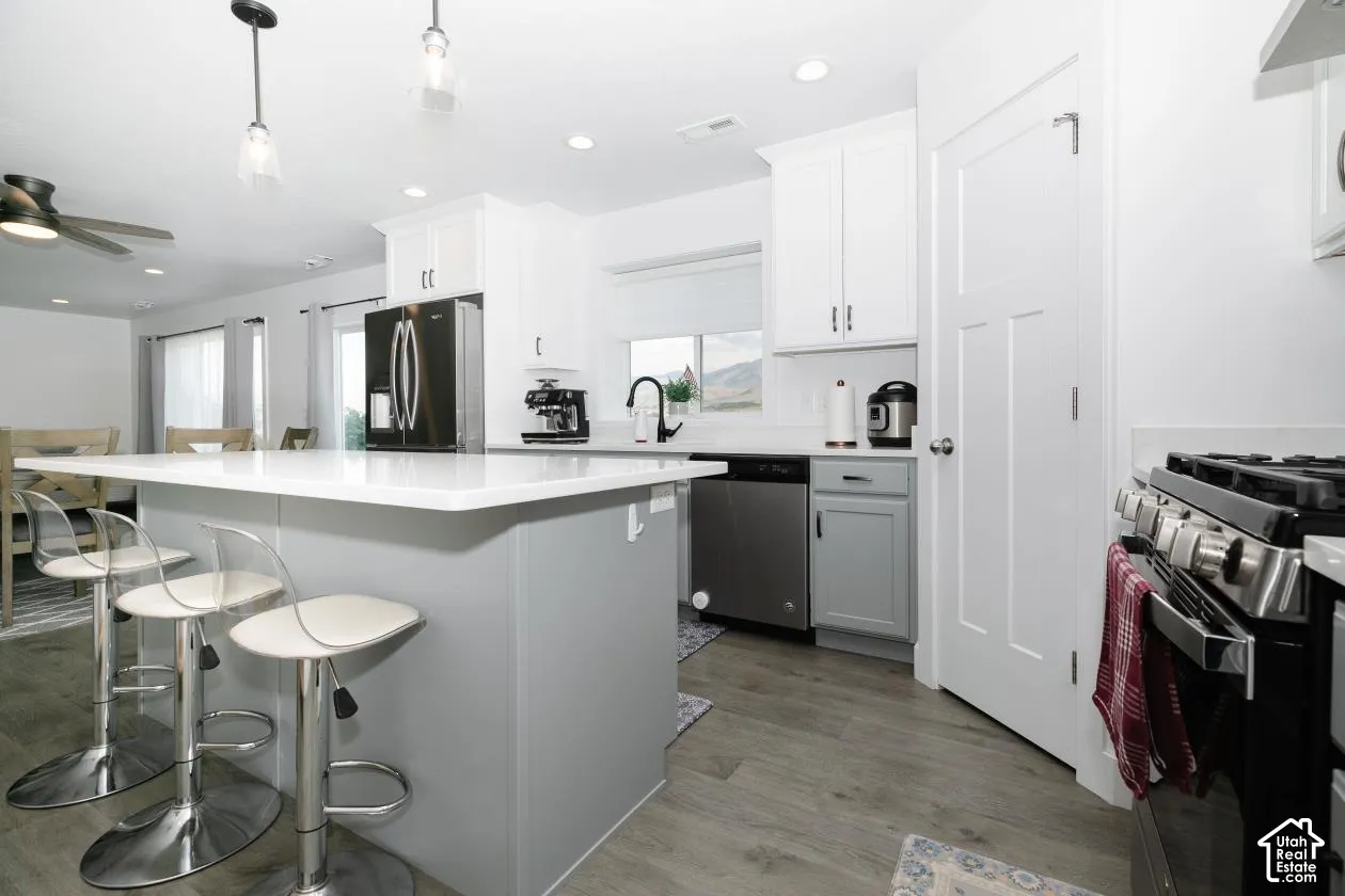 Contemporary kitchen featuring a large island with a light countertop, white upper cabinetry, and stainless steel appliances
