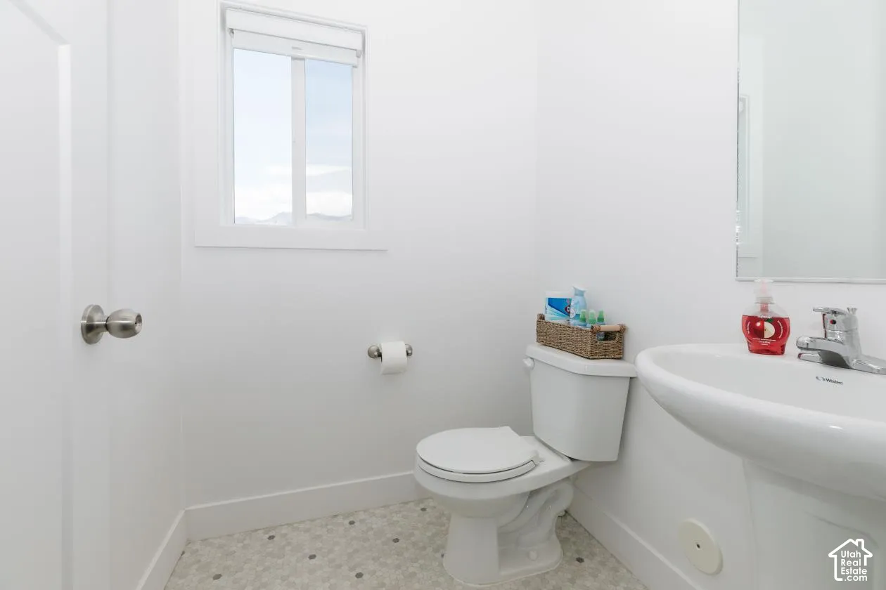 A Half Bathfeaturing a pedestal sink, white toilet, and window coming into house by mudroom and garage