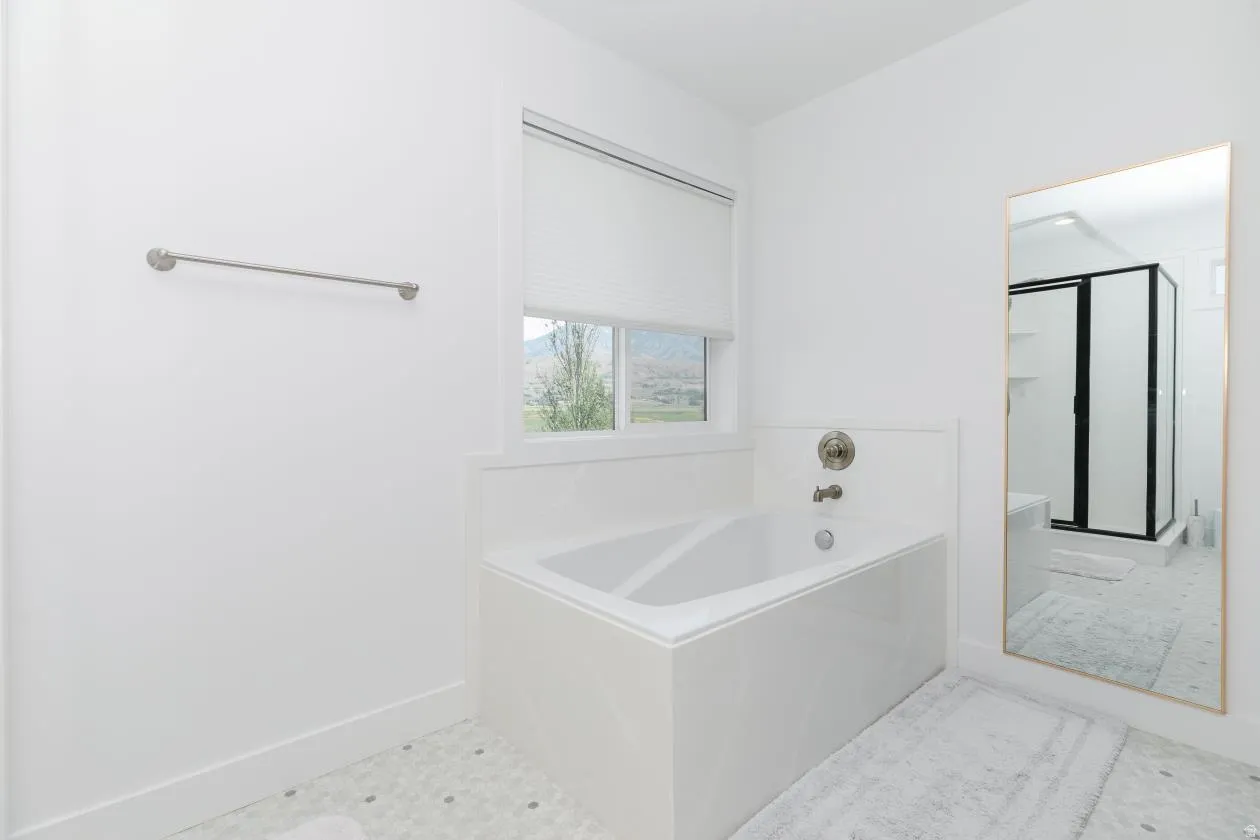 White-tiled bath with a chrome faucet and a window featuring a white blind