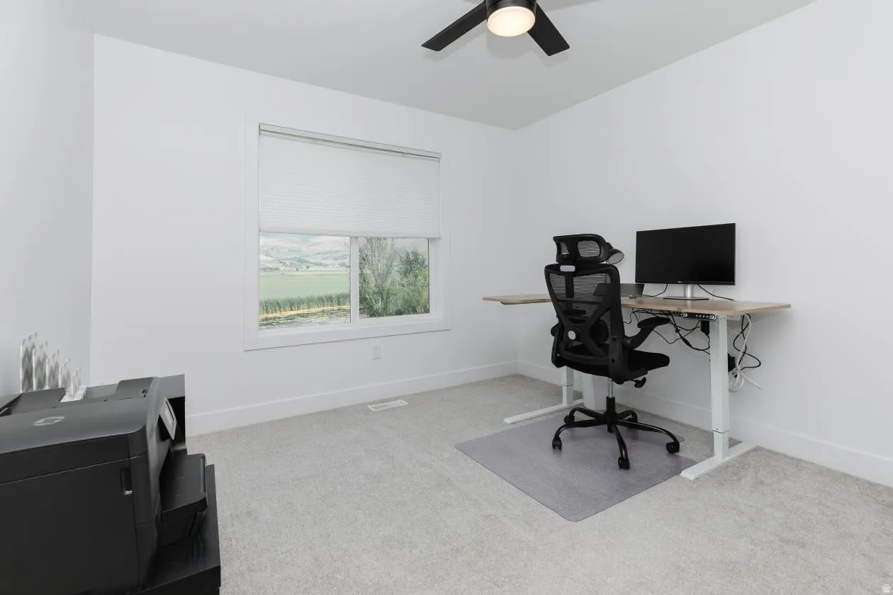 Light-filled room featuring a single window with blinds, a black ceiling fan, and light-toned wall-to-wall carpeting