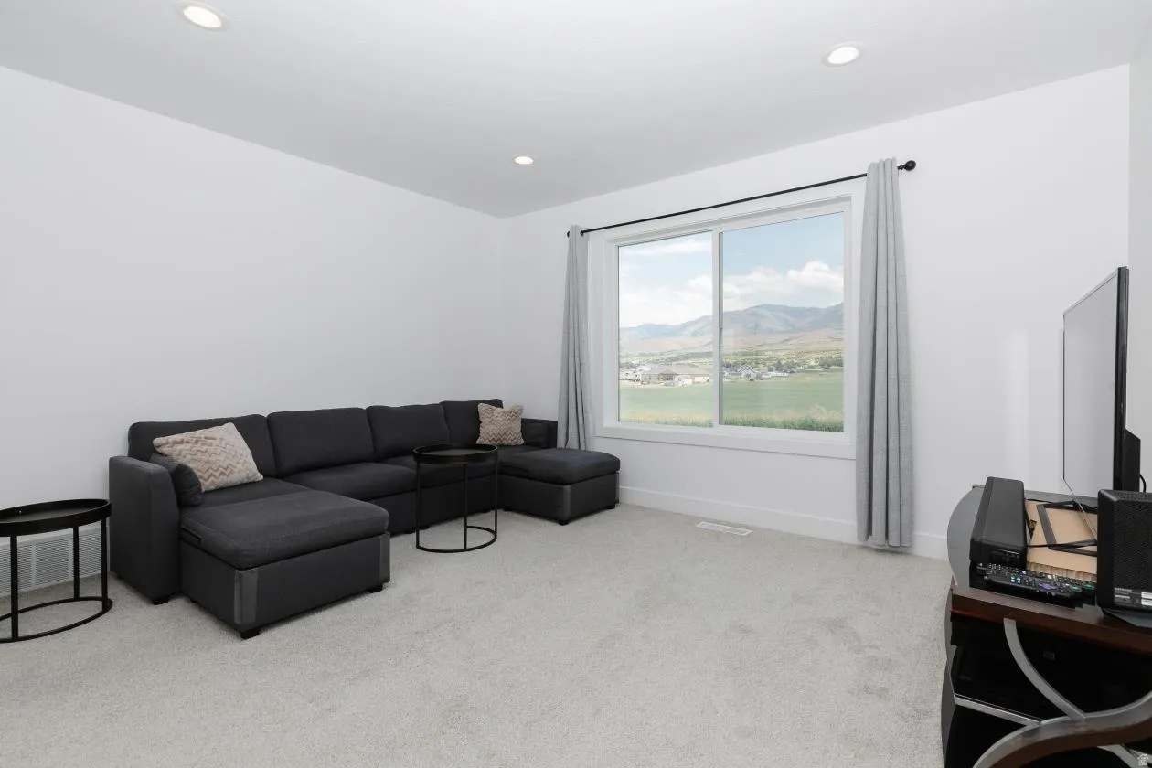 Spacious room featuring light gray carpeting, recessed ceiling lighting, a large window with white trim, and white baseboards right at the top of the stairs