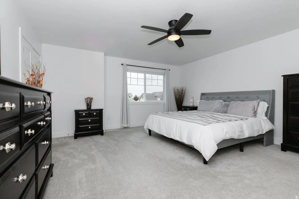 Spacious bedroom featuring light gray carpeting, crisp white walls, and a multi-pane window with white trim