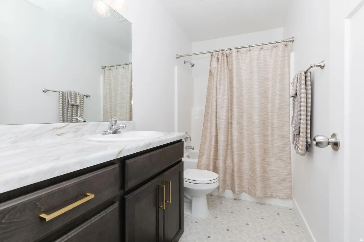 Bathroom featuring a dark wood-finish vanity with golden hardware, a solid surface countertop, an undermount sink, and an integrated shower and tub with a shower curtain rod