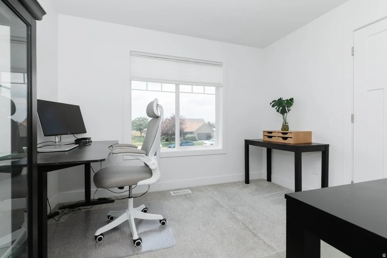Bright interior room featuring a large window, light-colored carpeting, white walls, and a white interior door