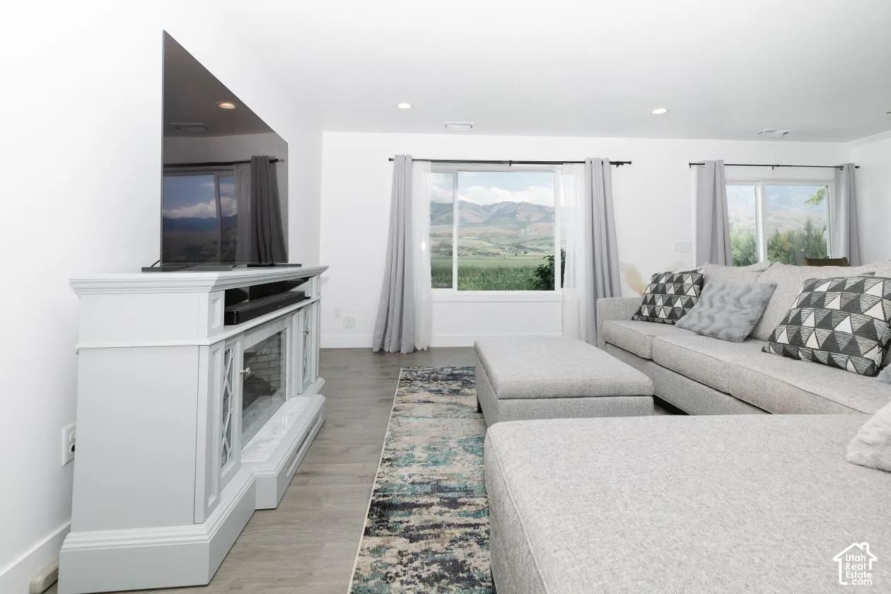 Bright living space featuring expansive windows, wood-finish flooring, recessed lighting, and a decorative fireplace console