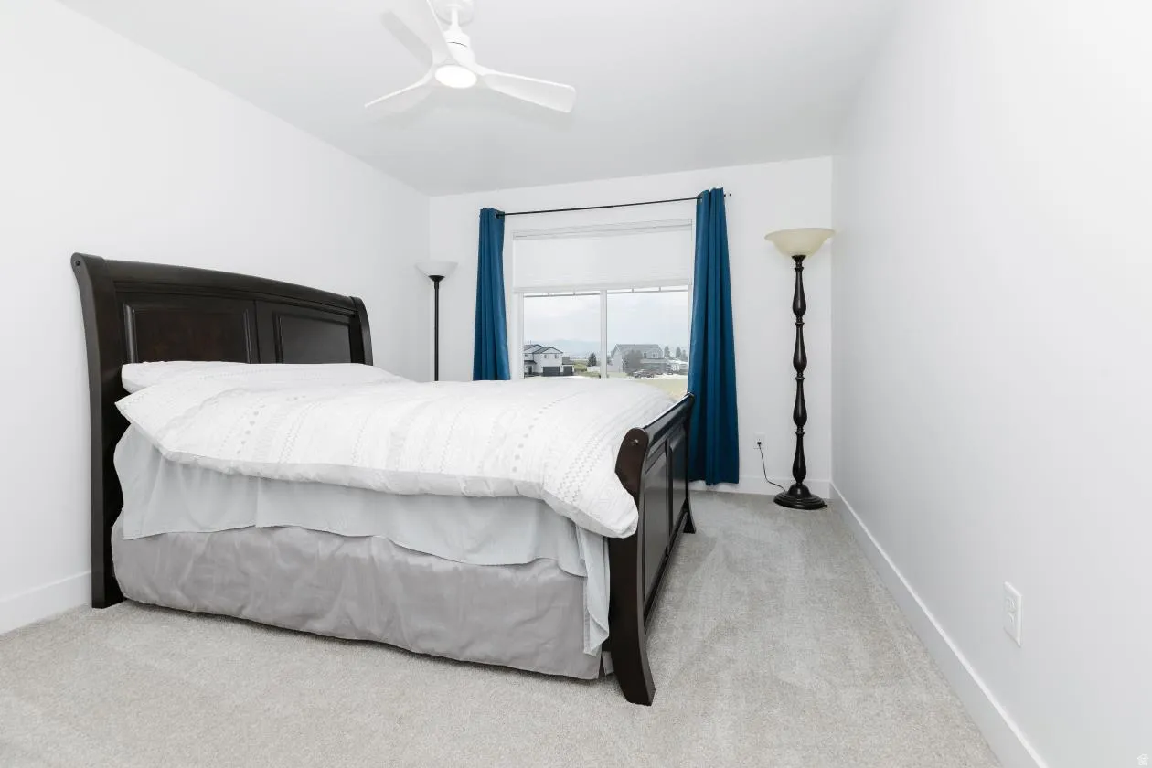 Bedroom featuring light gray carpet, white walls, a large window with blue drapes, and a ceiling fan