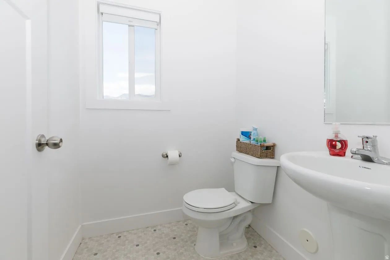 A Half Bathfeaturing a pedestal sink, white toilet, and window coming into house by mudroom and garage