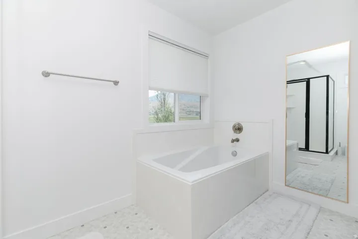 White-tiled bath with a chrome faucet and a window featuring a white blind