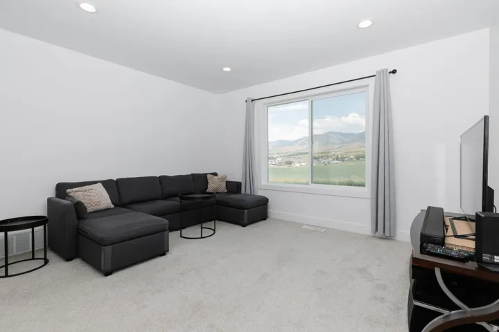Spacious room featuring light gray carpeting, recessed ceiling lighting, a large window with white trim, and white baseboards right at the top of the stairs