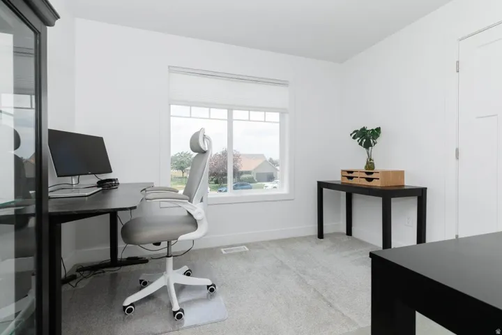 Bright interior room featuring a large window, light-colored carpeting, white walls, and a white interior door