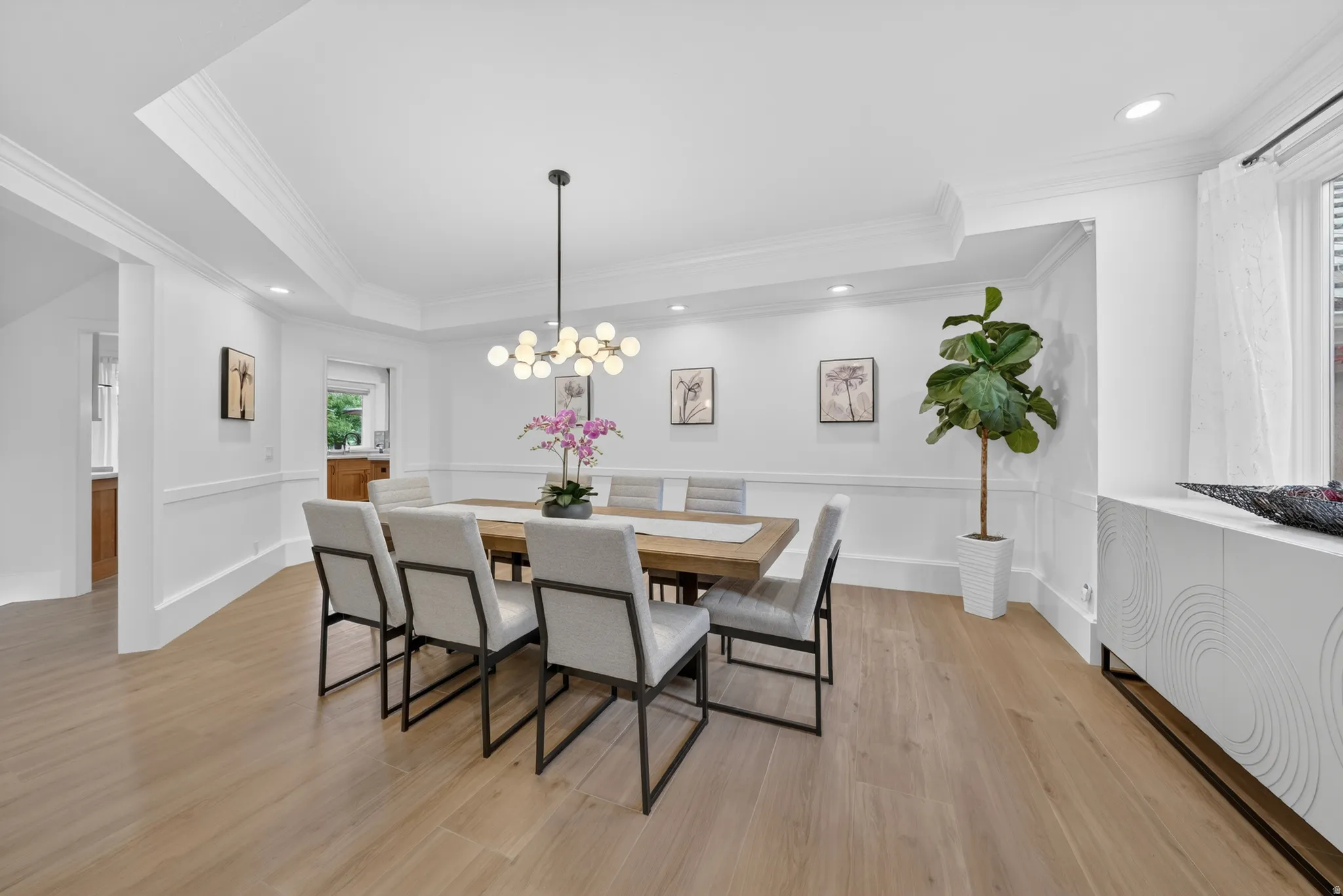 Dining area featuring light wood-finish flooring, white paneled walls, and layered crown molding
