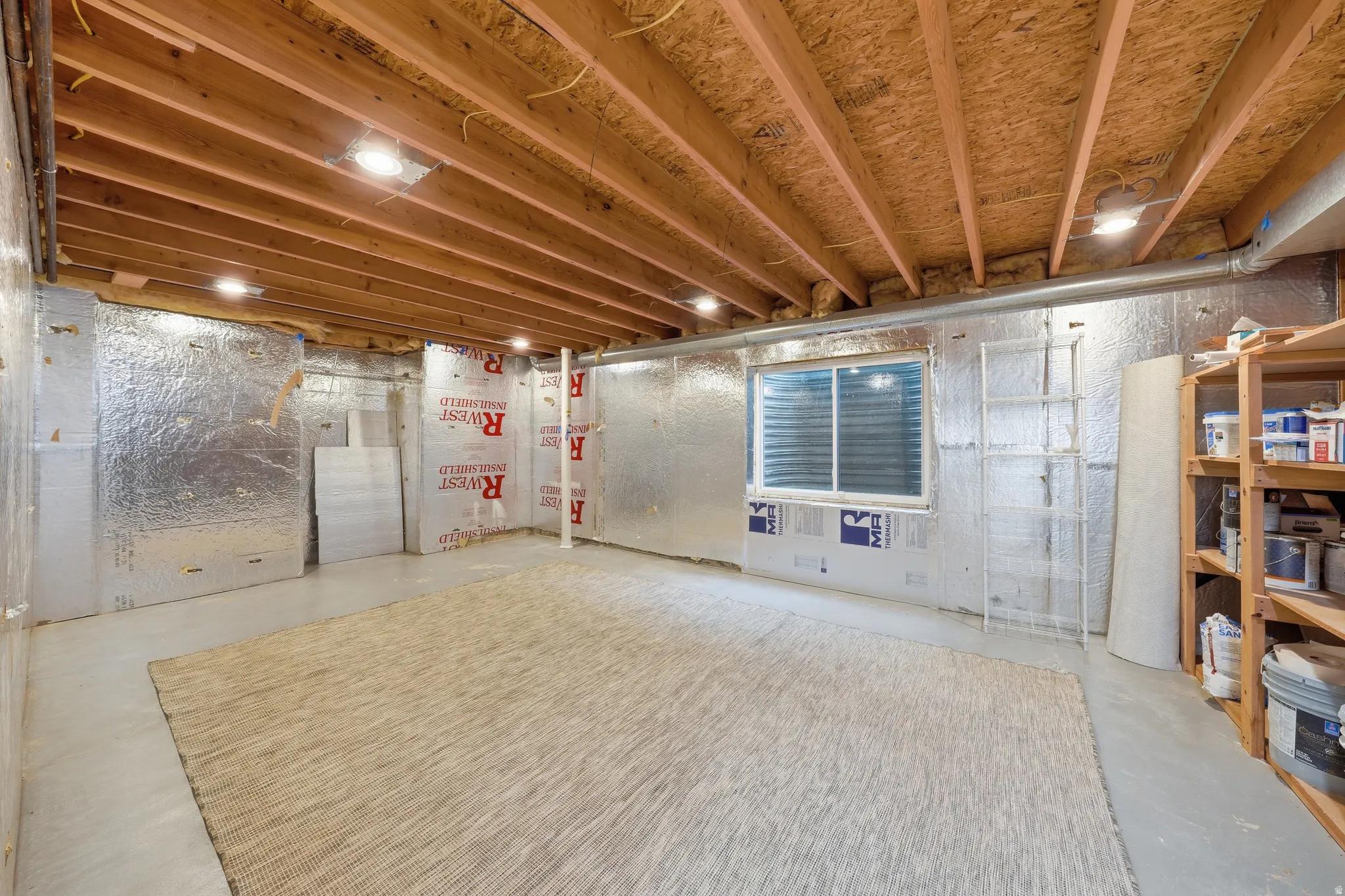 Unfinished basement space featuring exposed wood joists and subfloor, recessed lighting, foil-faced insulation, concrete flooring, and a single window