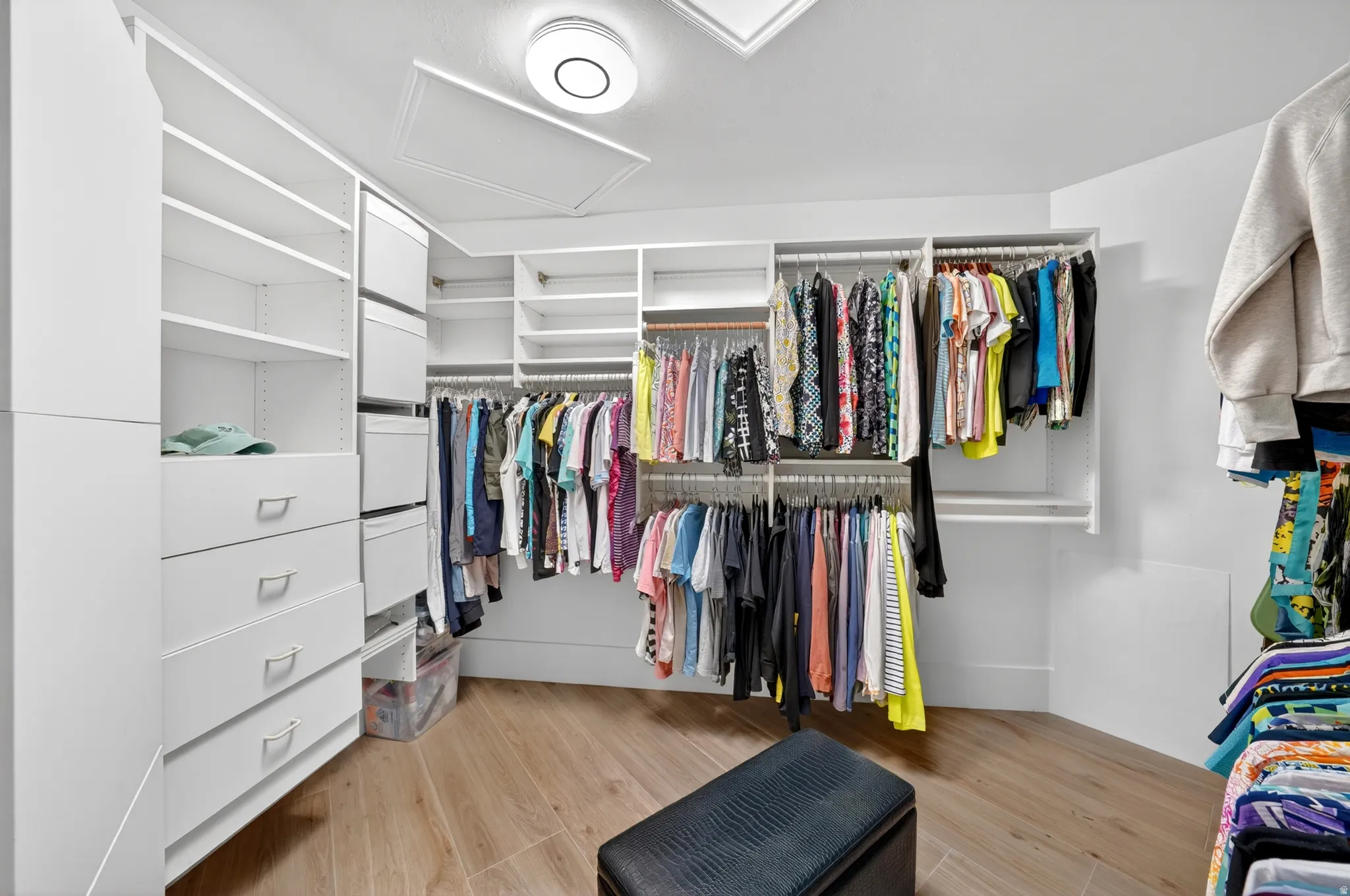 Walk-in closet featuring extensive built-in storage with shelves and drawers, multiple hanging rods, wood-finish flooring, and a flush-mount ceiling light