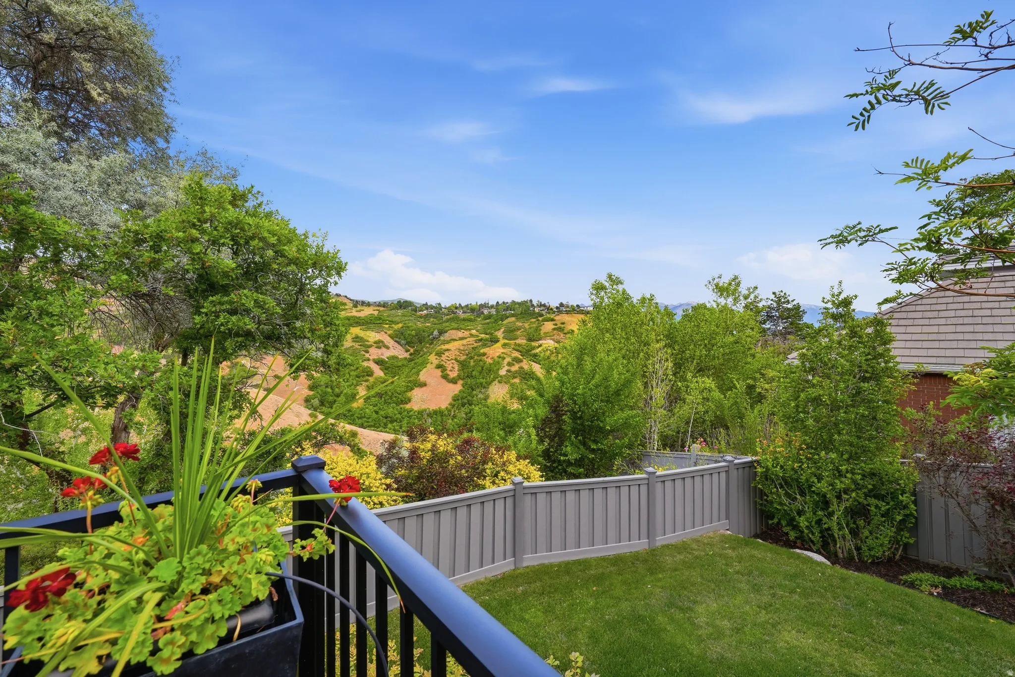 Expansive terraced backyard featuring a manicured lawn, a gray privacy fence, and mature trees
