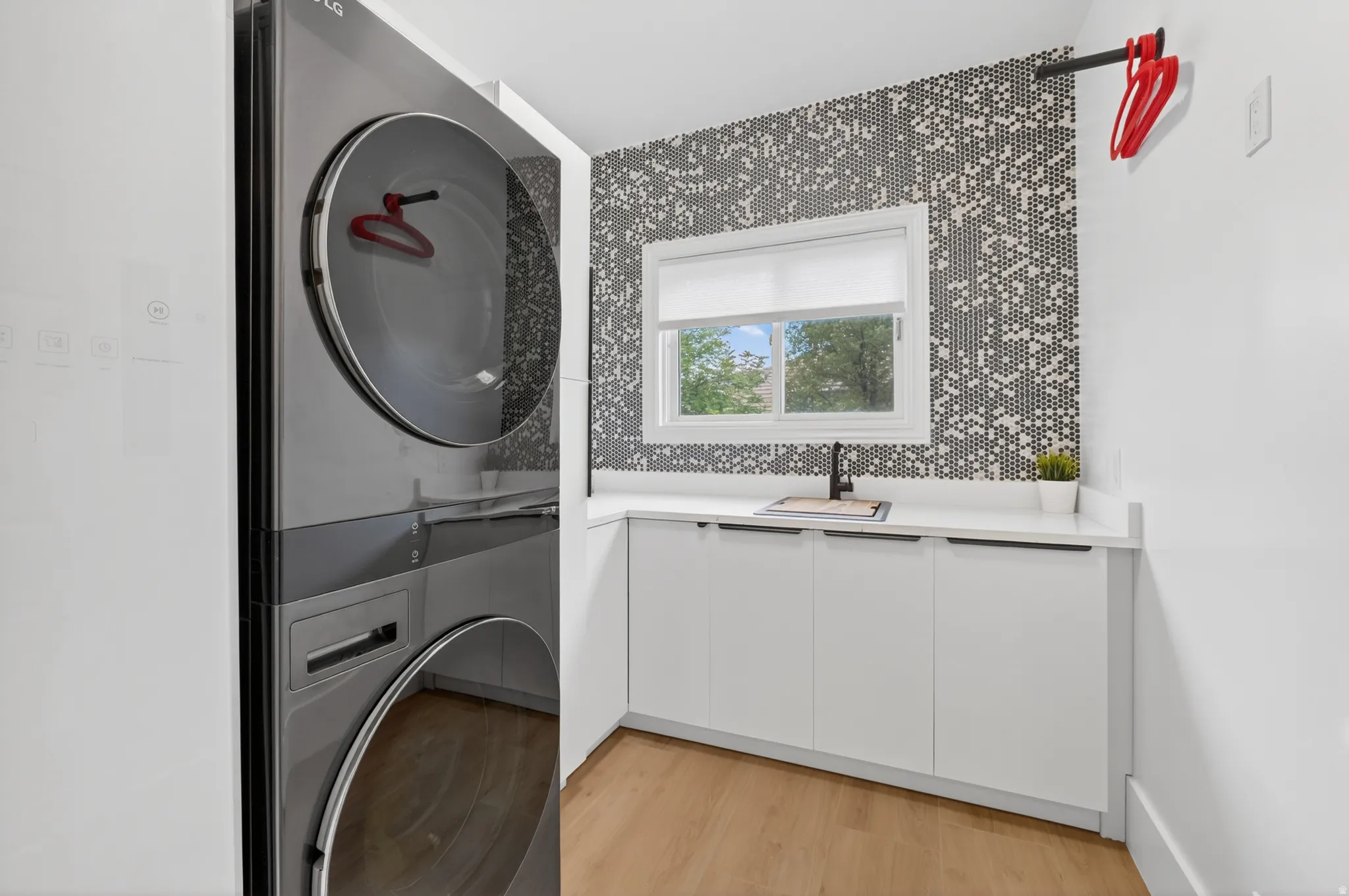 Integrated laundry station featuring stacked appliances, a built-in sink with a matte black faucet, and white cabinetry