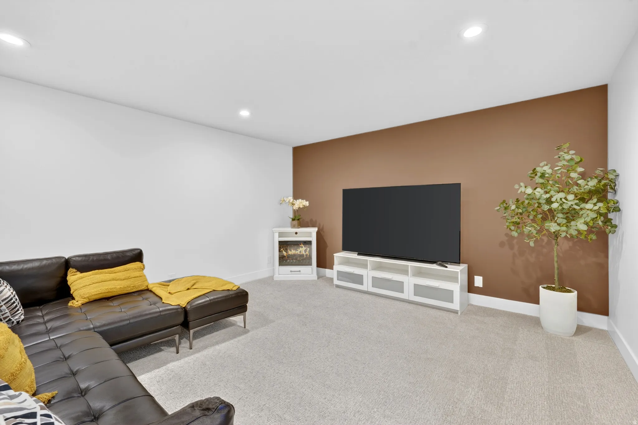 Spacious room with plush carpet flooring, recessed lighting, white baseboards, and a feature wall in a warm brown tone