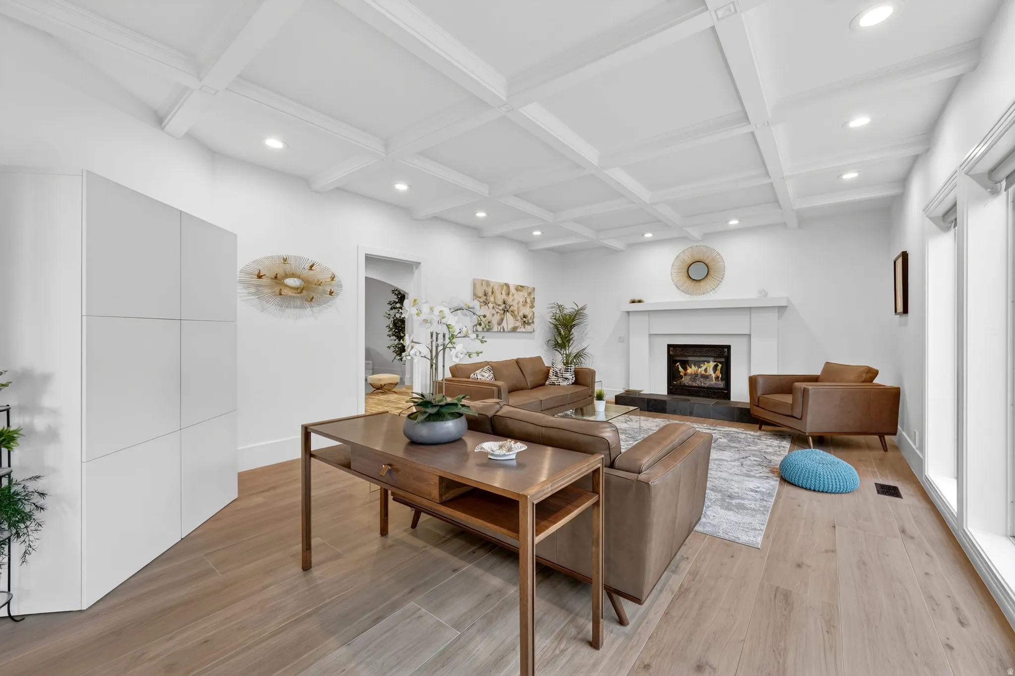 Bright living space featuring coffered ceilings with recessed lighting, a fireplace with a white mantel and dark stone surround, and wood-finish flooring