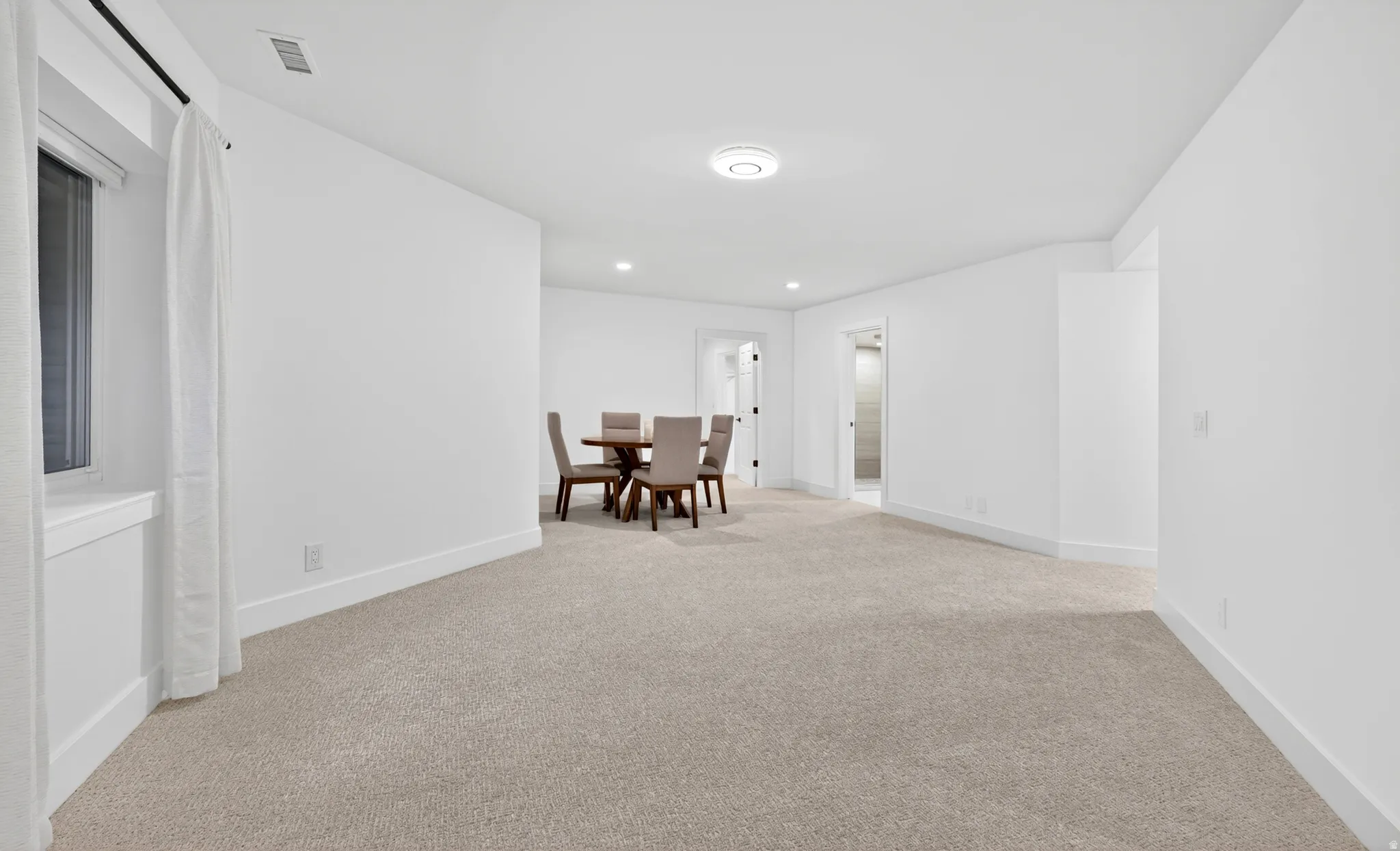 Spacious room featuring light-colored carpeting, white walls, and a round overhead light fixture