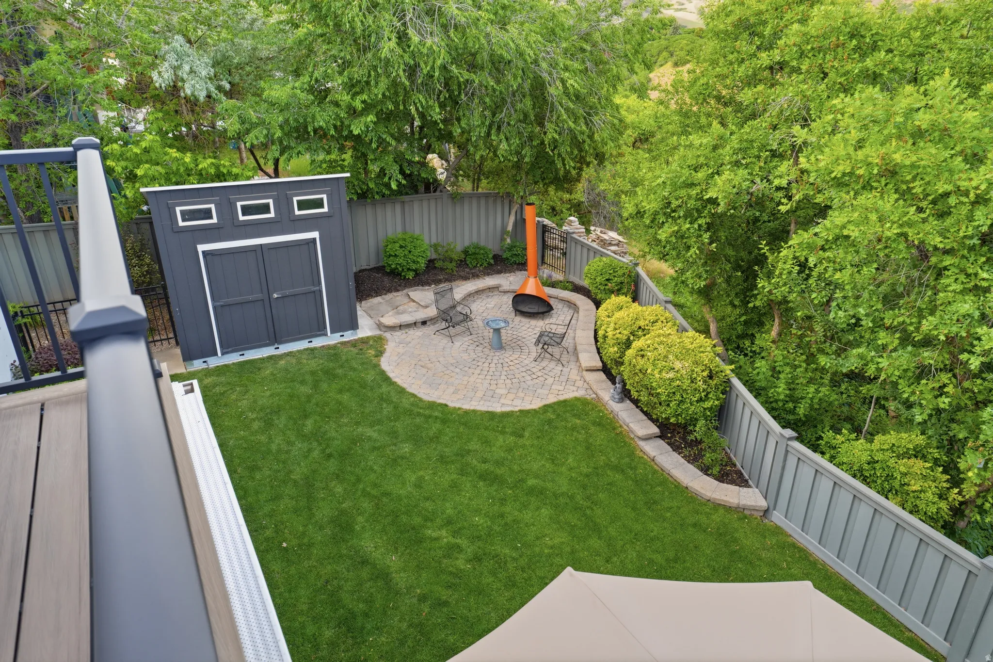 Manicured backyard featuring a paver patio, mature landscaping, a modern storage shed, privacy fencing, and wood-finish decking