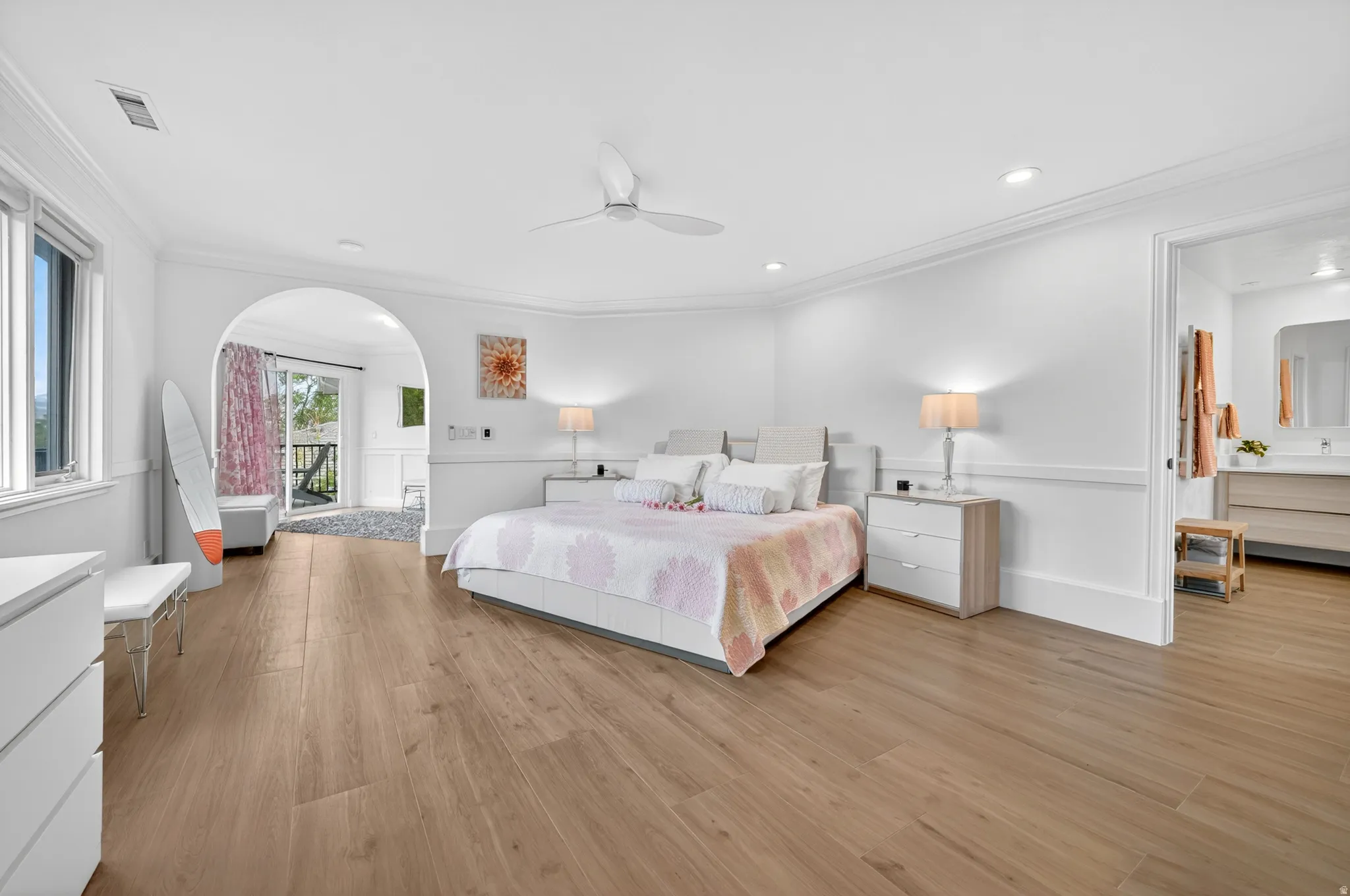 Spacious room featuring wood-finish flooring, an arched doorway, and crown molding
