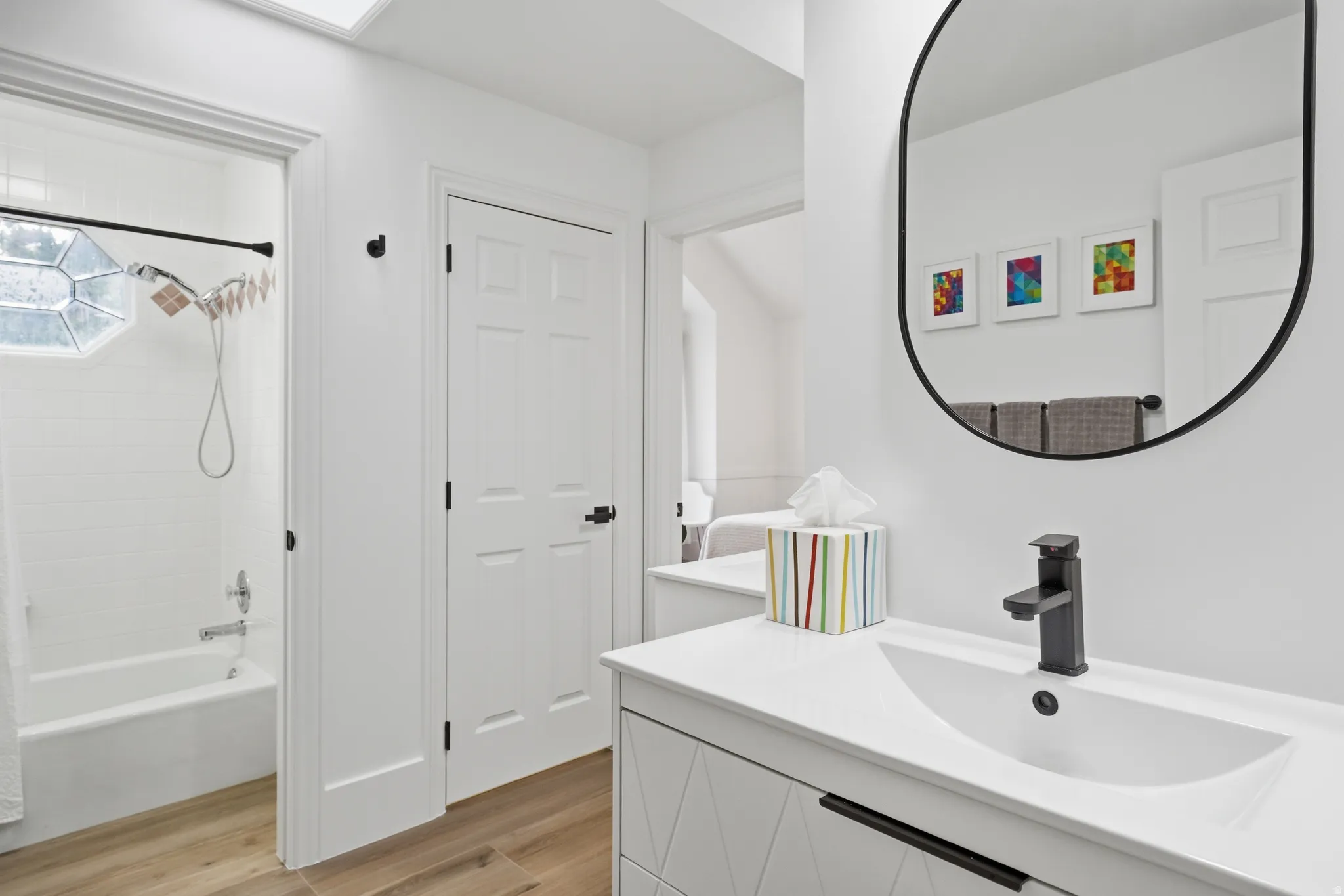 Modern bathroom featuring a white vanity with integrated sink, black matte faucet, and an oval-framed mirror