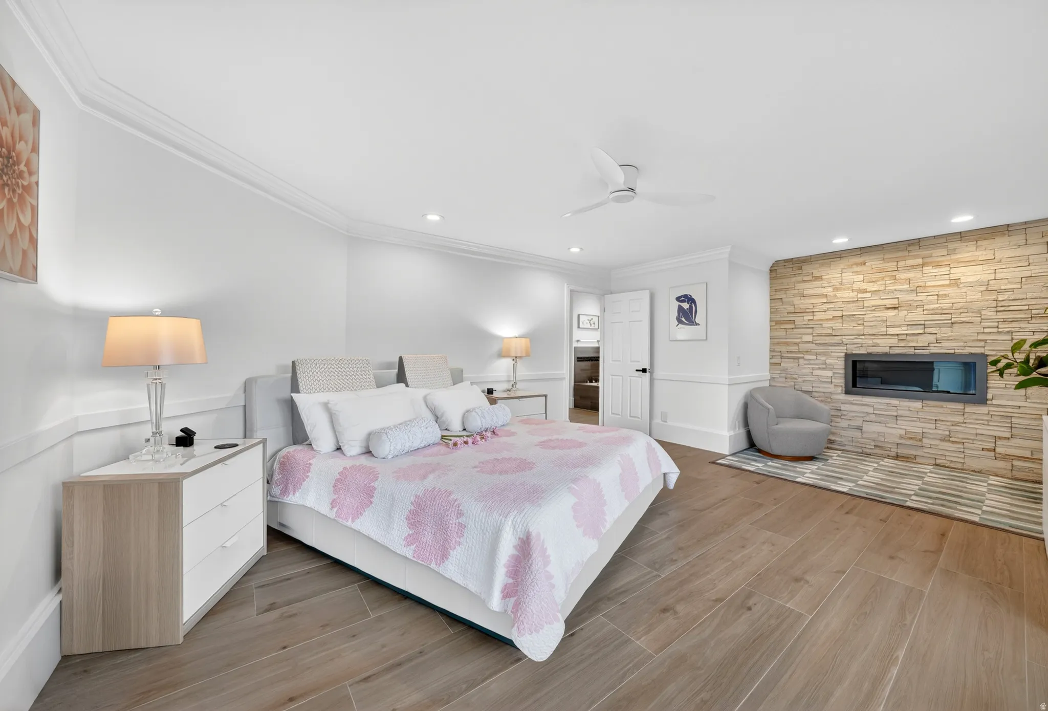 Spacious room featuring wood-finish flooring, a contemporary fireplace with a stacked stone surround, recessed lighting, and crown molding