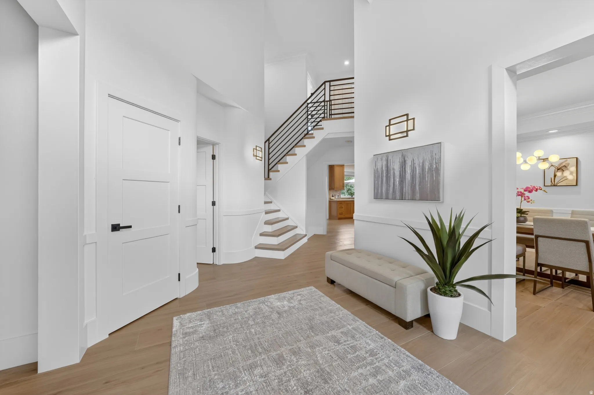 Grand entryway featuring a prominent staircase with black horizontal balusters, light wood-finish flooring, and white paneled walls