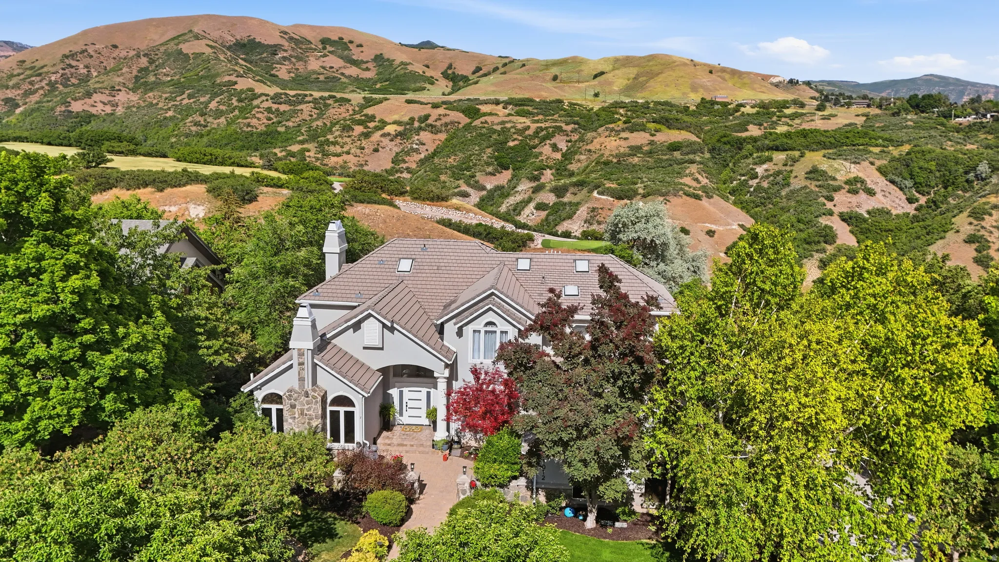 Expansive property with a light gray exterior, a multi-gabled roof, and stone-clad chimneys
