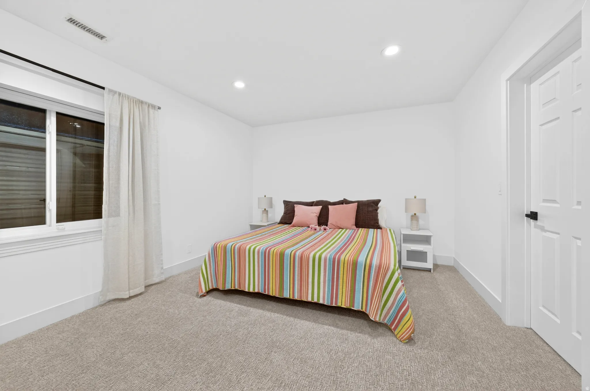 Carpeted room featuring a white paneled door with black hardware, a window with white trim, and recessed ceiling lighting