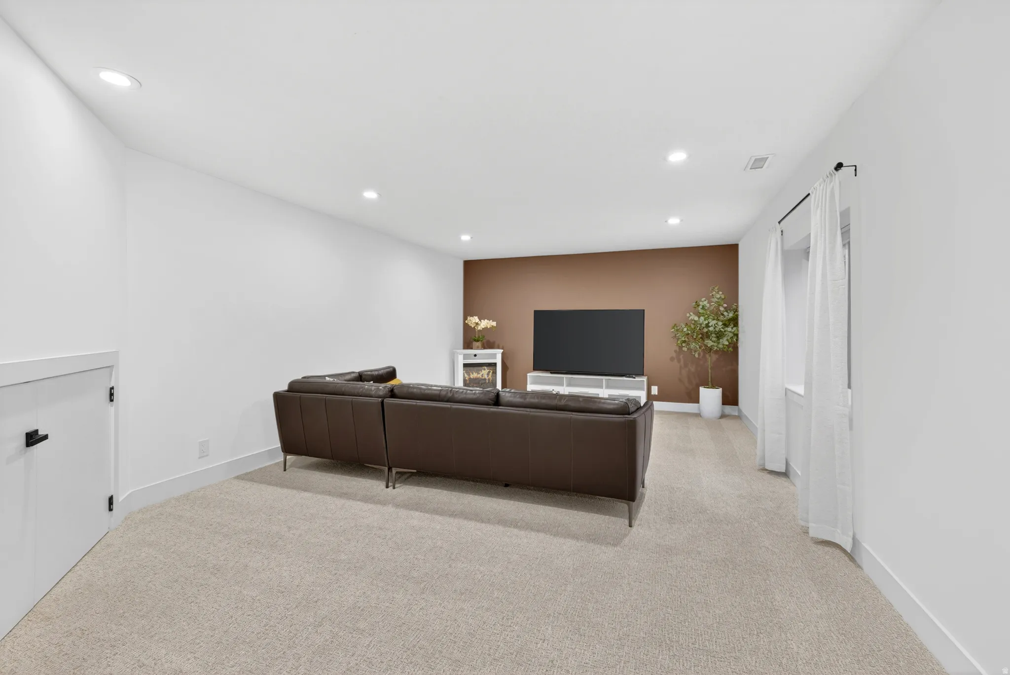 Spacious carpeted room featuring recessed lighting, a window with sheer white curtains, and a brown accent wall