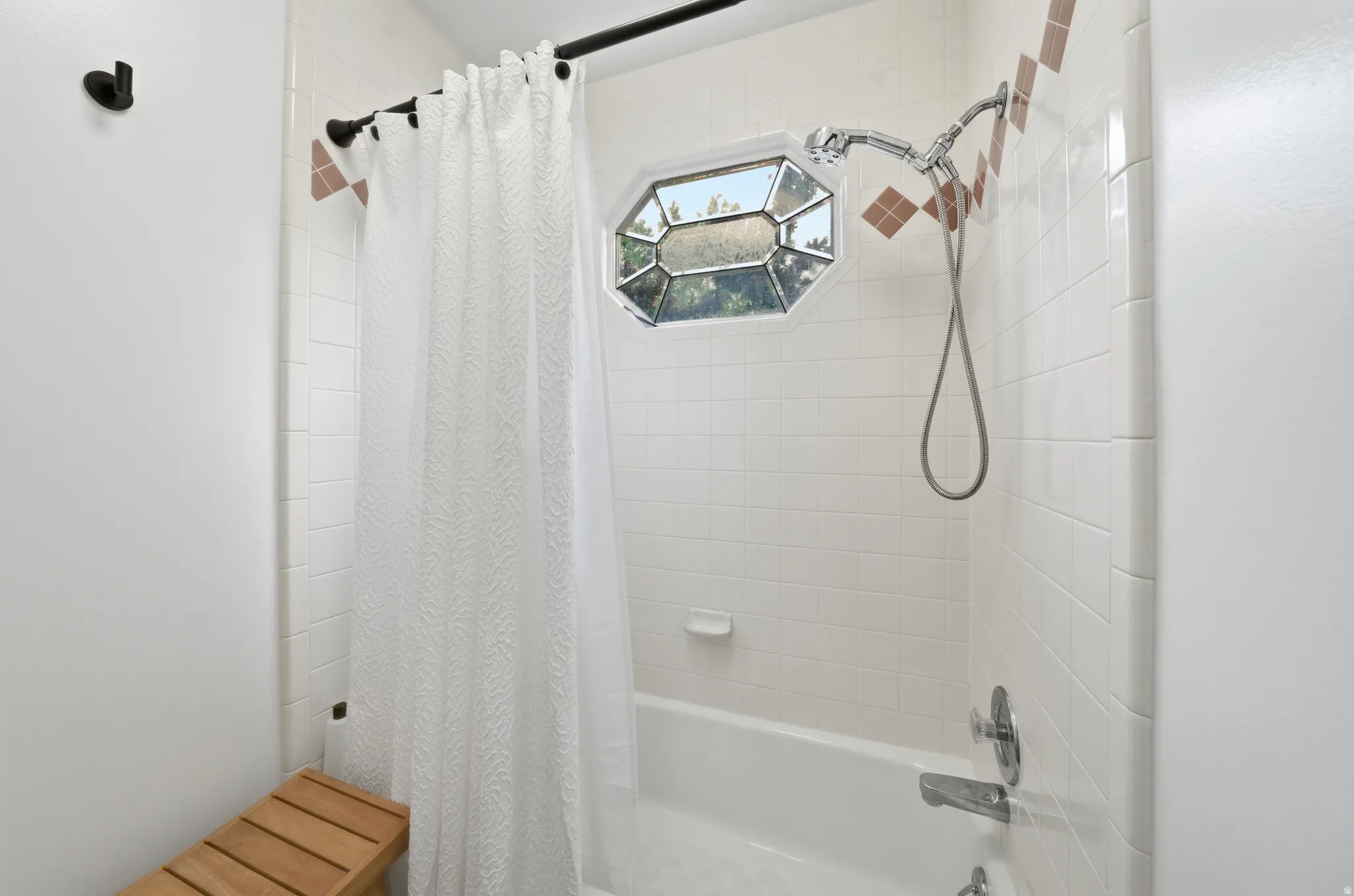Bathtub with white subway tile surround, accent tile detailing, and an octagonal window