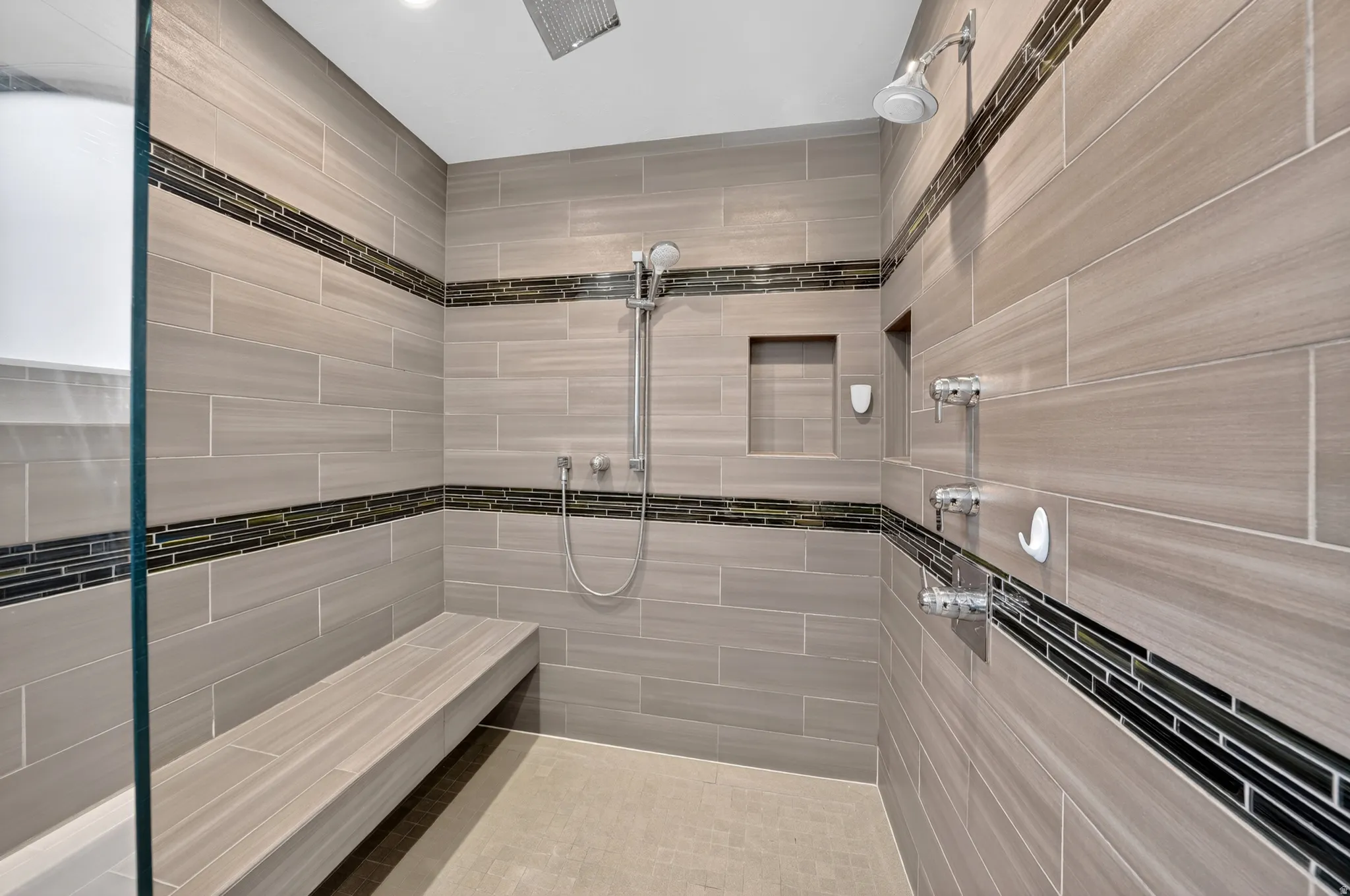 Spacious shower enclosure featuring light-toned tile, a built-in bench, and a dual shower head system