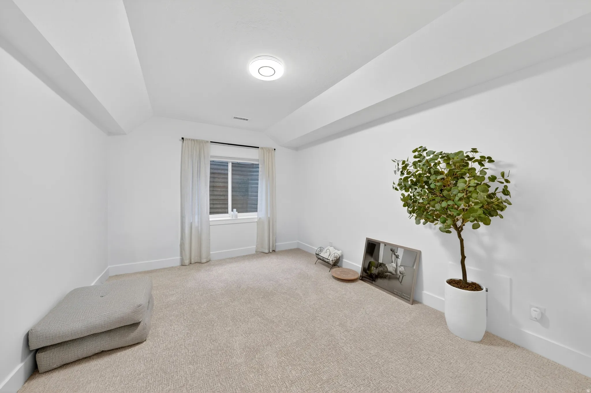 Carpeted room featuring a single window with blinds and sheer curtains, white walls, and a contemporary ceiling light fixture