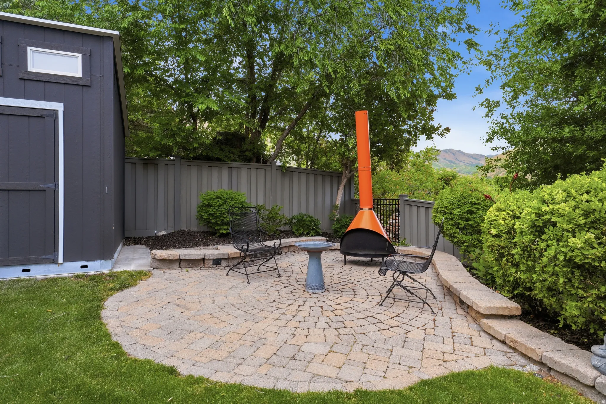 Circular paver patio with a stone retaining wall, bordering a manicured lawn