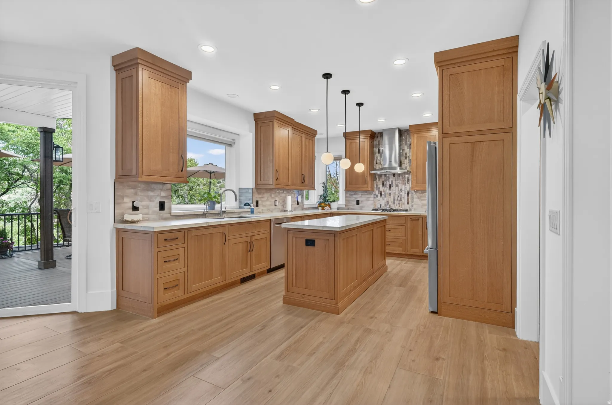 Modern kitchen featuring wood-finish flooring, light wood cabinetry, white countertops, and a tiled backsplash