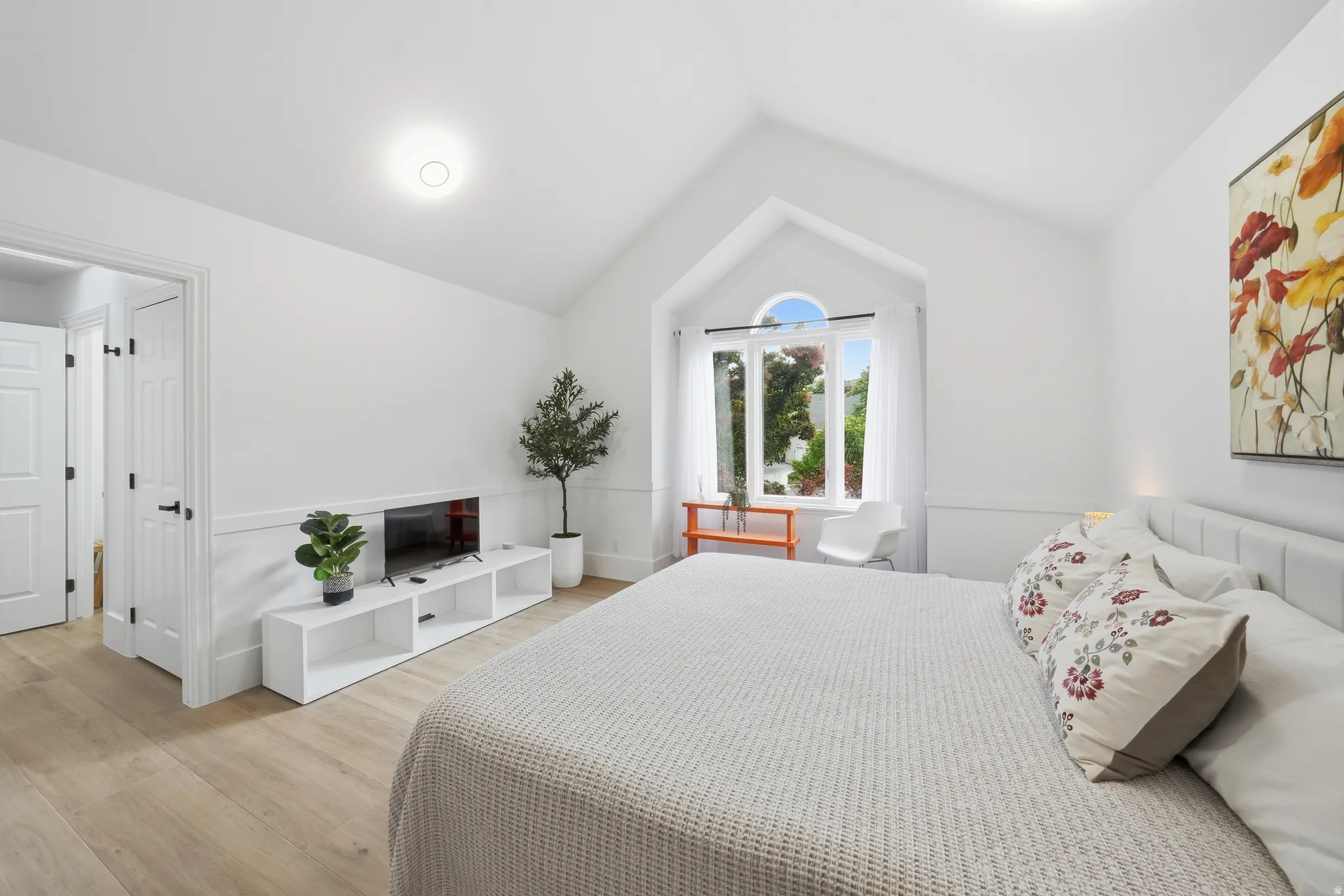 Vaulted ceiling room featuring light wood-finish flooring and white wainscoting