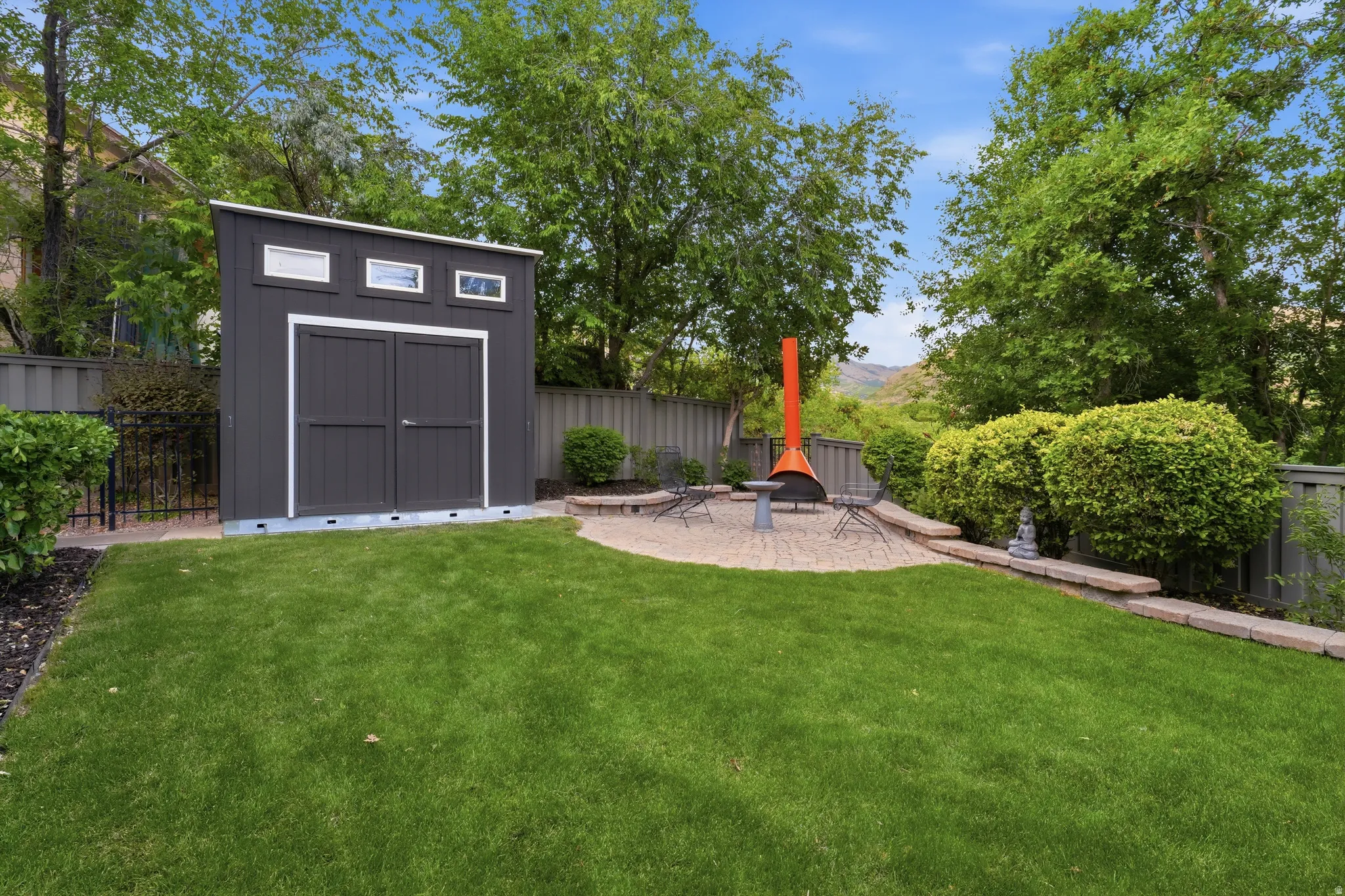 Landscaped backyard featuring a storage shed with transom windows, a pea gravel patio, and mature perimeter trees