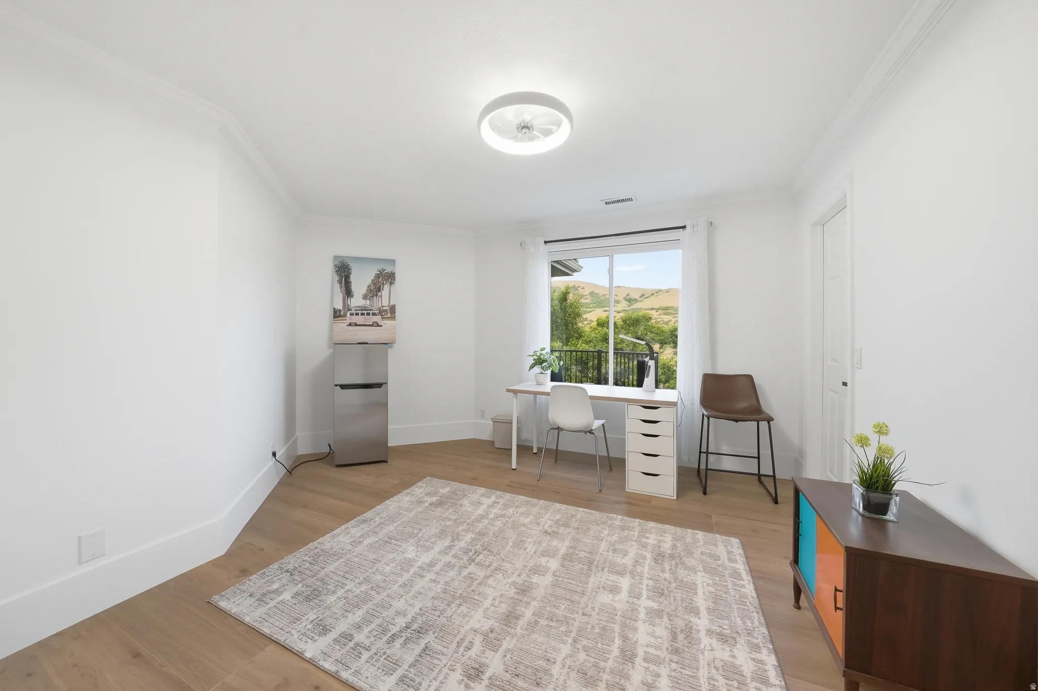 Room featuring wood-finish flooring, a contemporary ceiling light fixture, white crown molding, and a window with a mountain backdrop