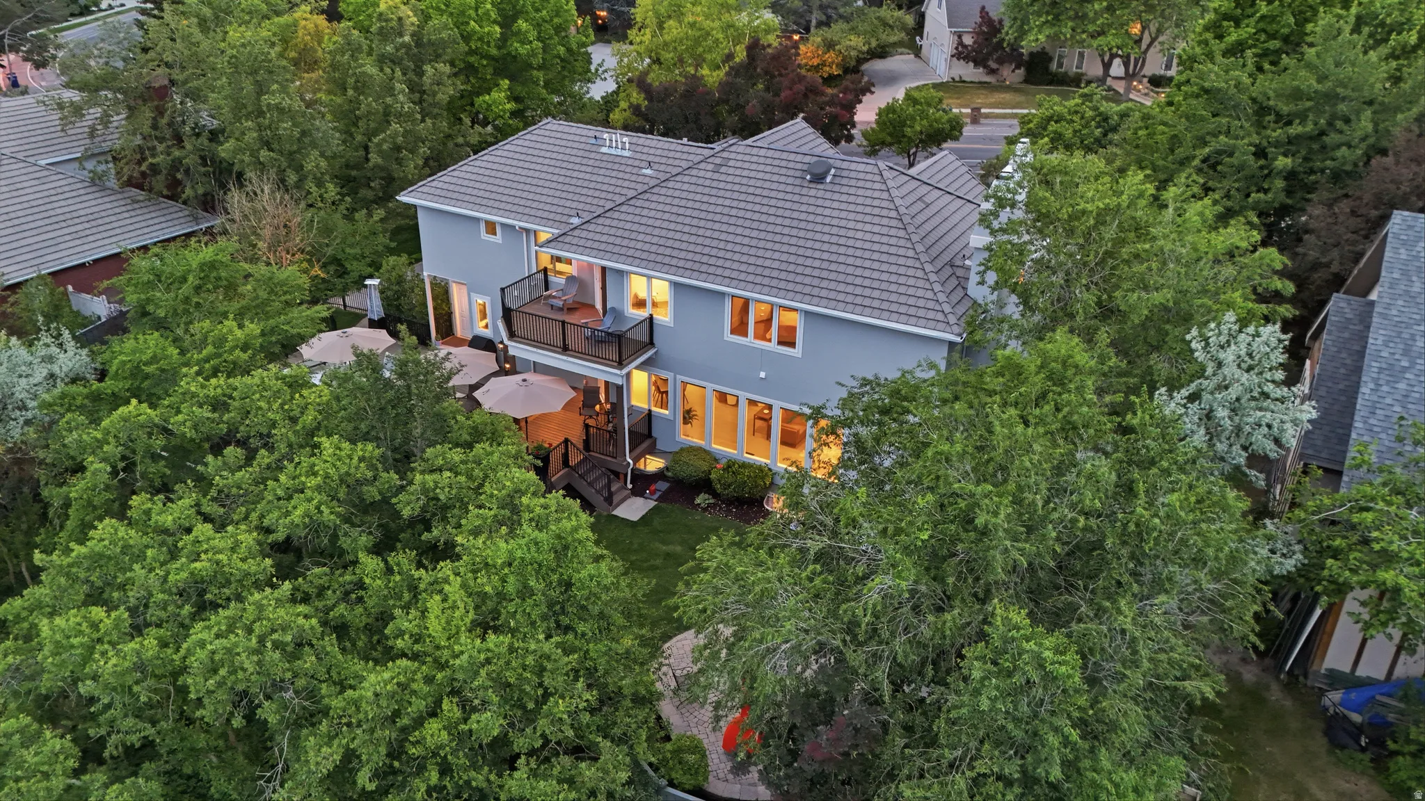 Rear exterior featuring a second-story balcony with glass railing, ground-level deck, stucco siding, and a tiled roof