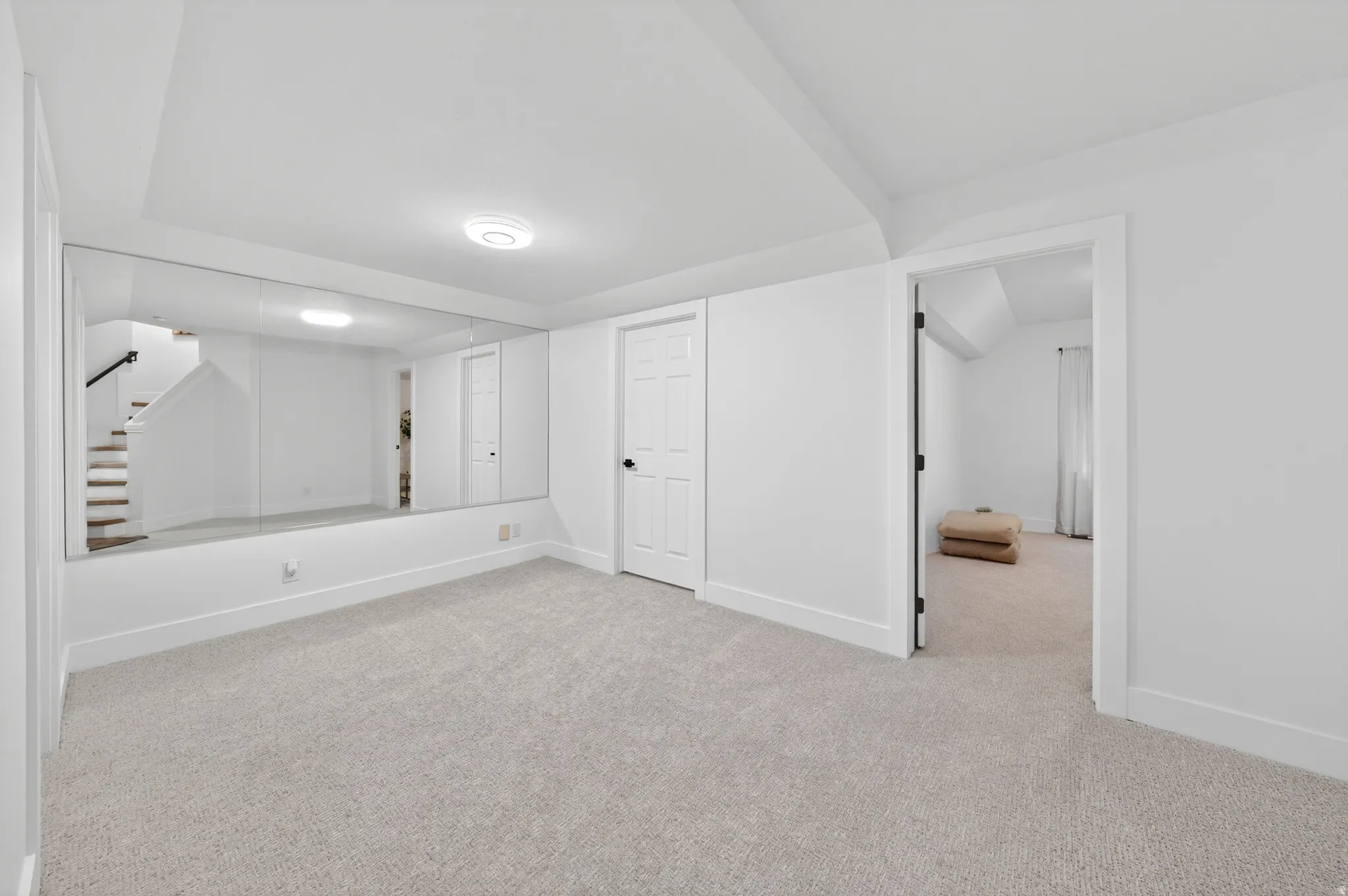 Spacious room featuring a full wall mirror, light-toned carpeting, white walls, and a white paneled door