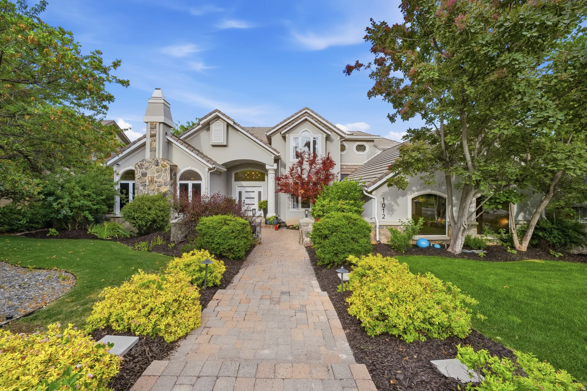 Stucco exterior with stone accents, a brick paver walkway, arched windows, and mature landscaping
