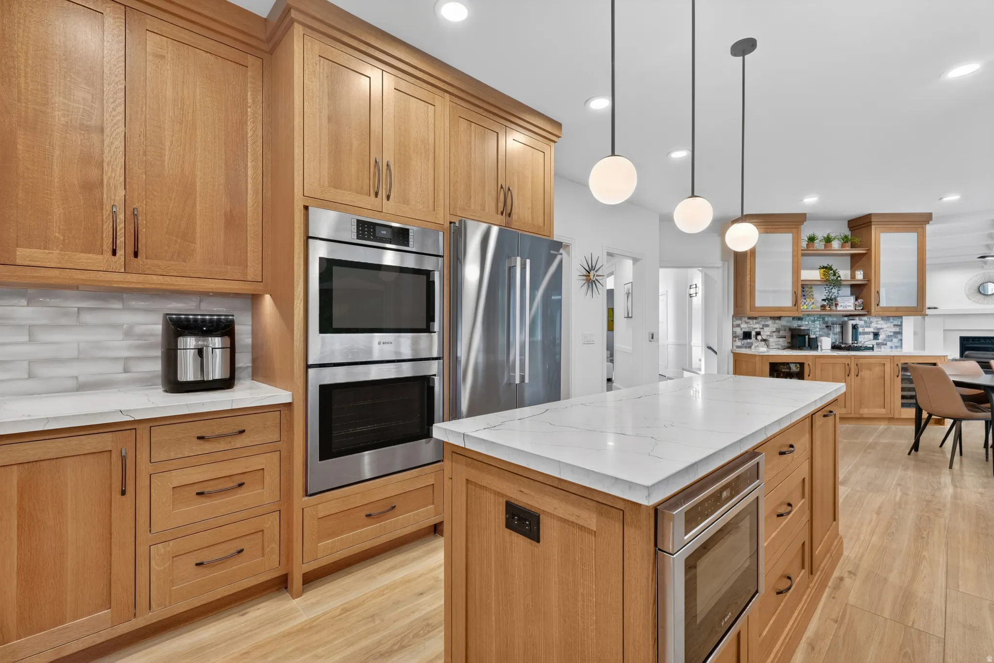 Contemporary kitchen featuring a large central island with a white countertop, recessed lighting, wood-finish flooring, custom wood cabinetry, and stainless steel appliances