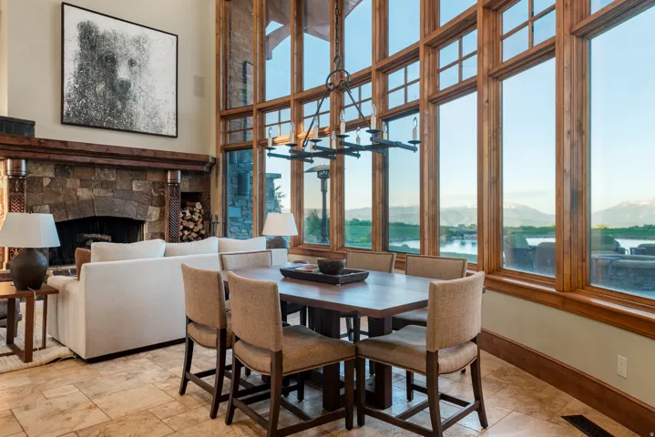 Great room featuring a stone fireplace with a wood mantle, an adjacent dining area, and full-height windows