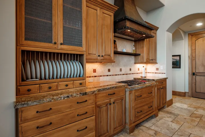 Gourmet kitchen with custom wood cabinetry, granite countertops, tile backsplash, built-in plate rack, and a gas range with a custom range hood