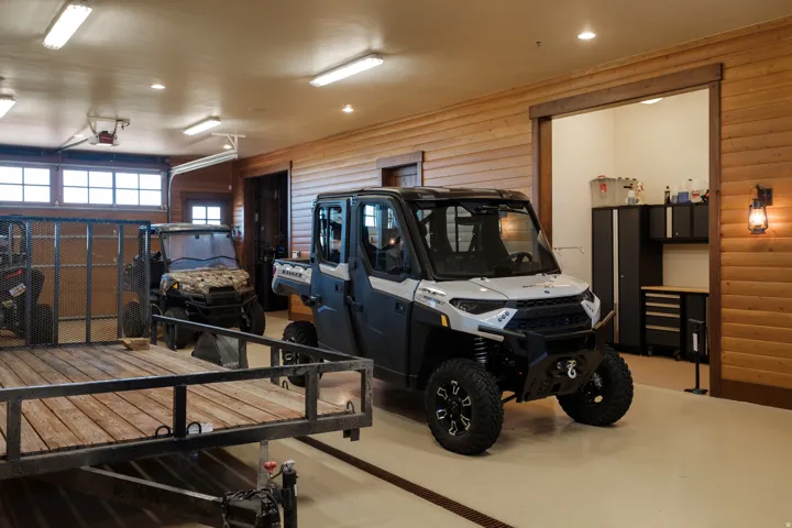 Spacious garage featuring light-toned flooring, wood-paneled walls, and overhead fluorescent lighting