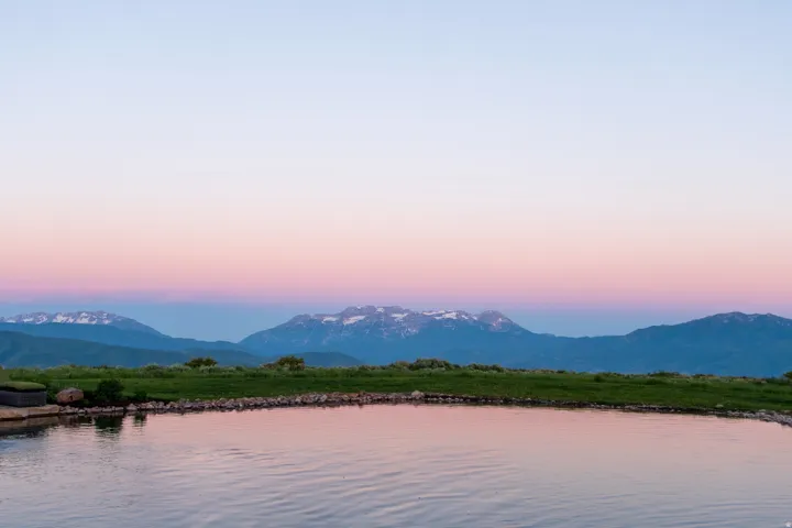 Reflecting pool with a stone edge, expansive green lawn, and distant snow-capped mountains