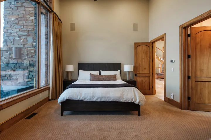 Spacious room featuring a bed with nightstands, large windows with natural wood trim, and two wood-paneled doors