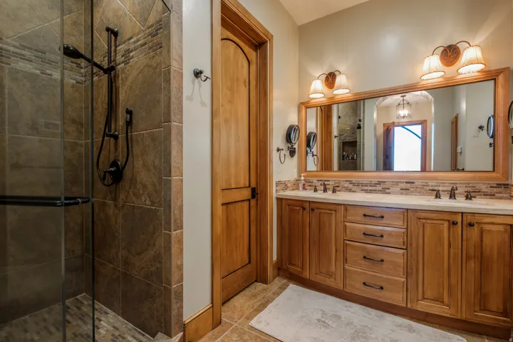 Double vanity with light wood cabinetry, stone countertops, and a full-width framed mirror