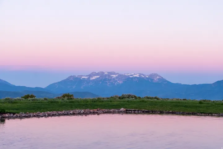 Body of water with a rocky bank and a distant mountain range featuring snow-capped peaks