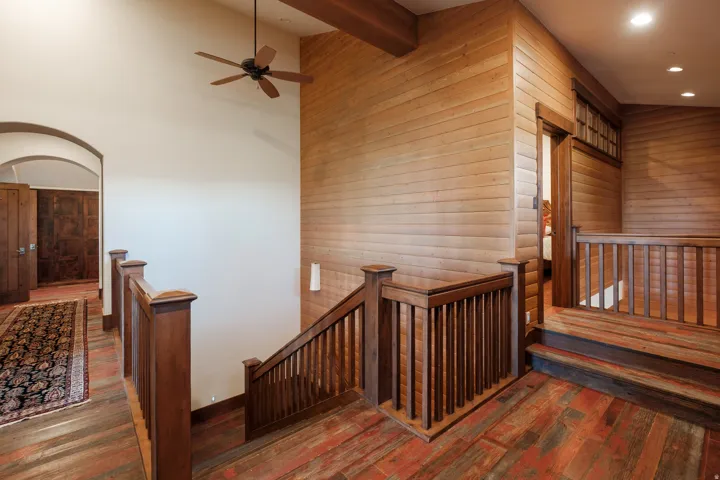 Wood-finish flooring throughout, featuring a staircase with wooden railings and a matching ceiling fan